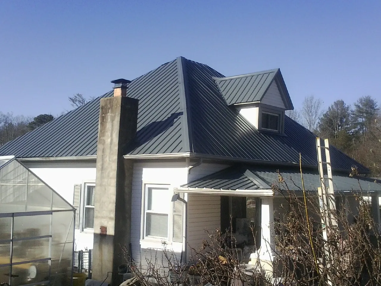 Dark blue standing seam metal roof on a white farmhouse with dormer — Slate & Tile Roof Repair by Roofing Brothers in Summit Point