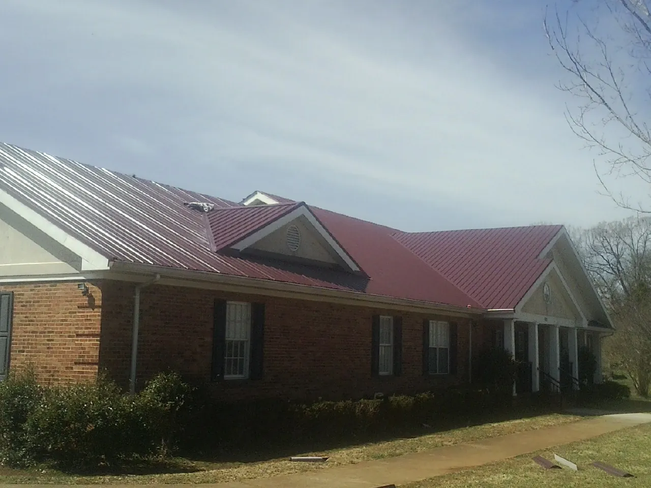 Red metal roof with gabled entries on a long brick building, from a Hail Damage Roof Repair job in Summit Point