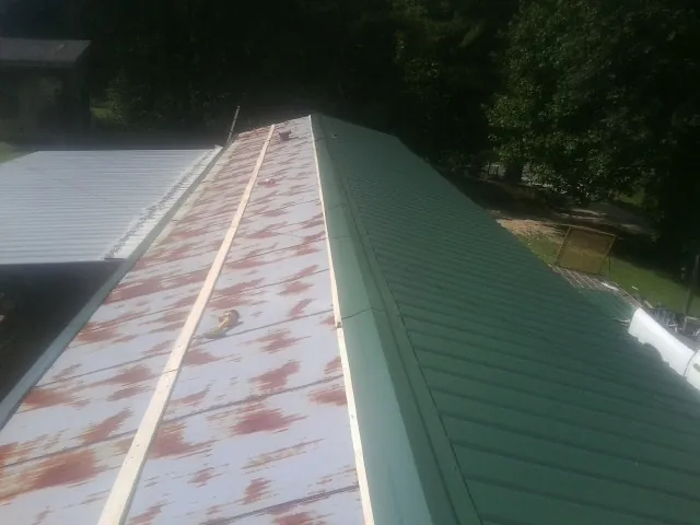 Old rusted panels beside newly installed green metal roofing — Wind Damage Roof Repair by Roofing Brothers in Summit Point