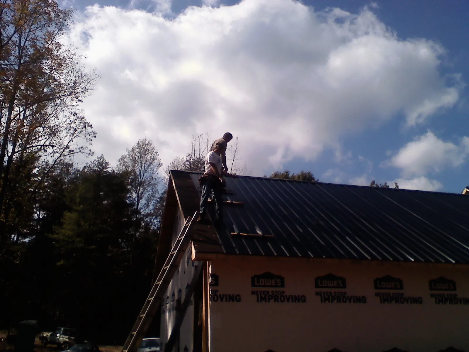Roofer fastening dark metal panels high against a cloudy sky, from a Roof Inspection job in Summit Point