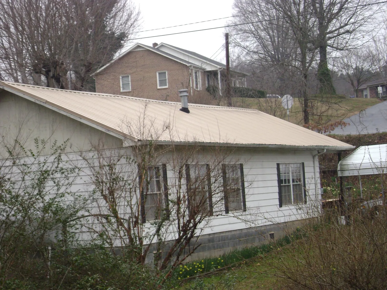 Tan metal roof on a white sided house set into a hillside — Commercial Roofing by Roofing Brothers in Summit Point